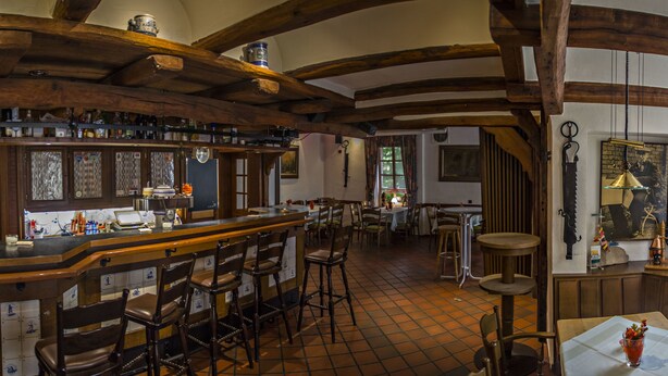 Zona de bar con vigas de madera, suelo de baldosas y taburetes.