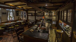Un restaurante acogedor con vigas de madera, varias mesas y sillas, una zona de bar y suelo de baldosas.