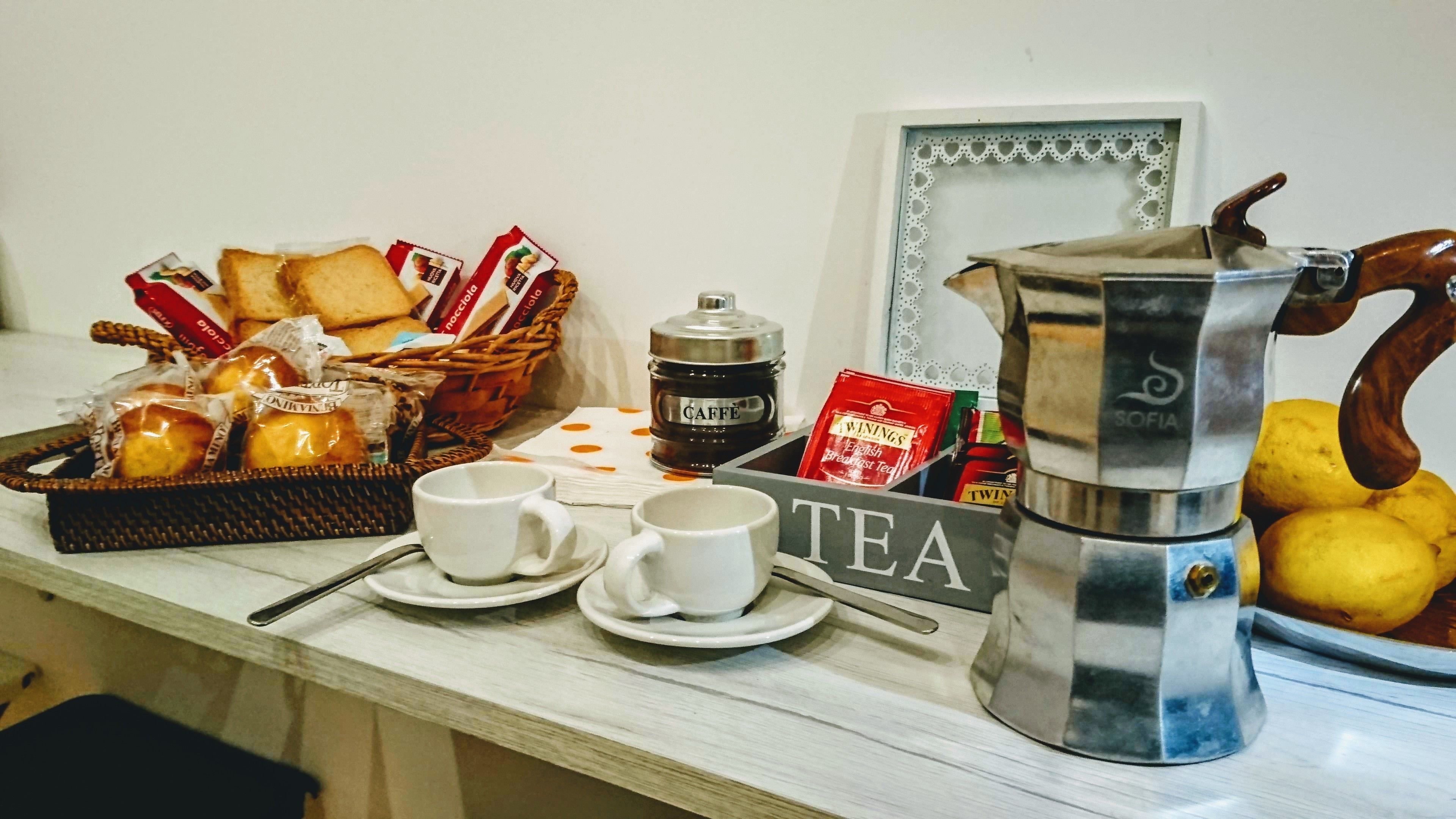 A breakfast setup with bread, pastries, coffee, tea, and lemons on a table.