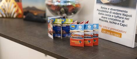 Um balcão com um letreiro de passeios de barco em Nápoles, um recipiente de vidro com lanches e vários folhetos de viagens.