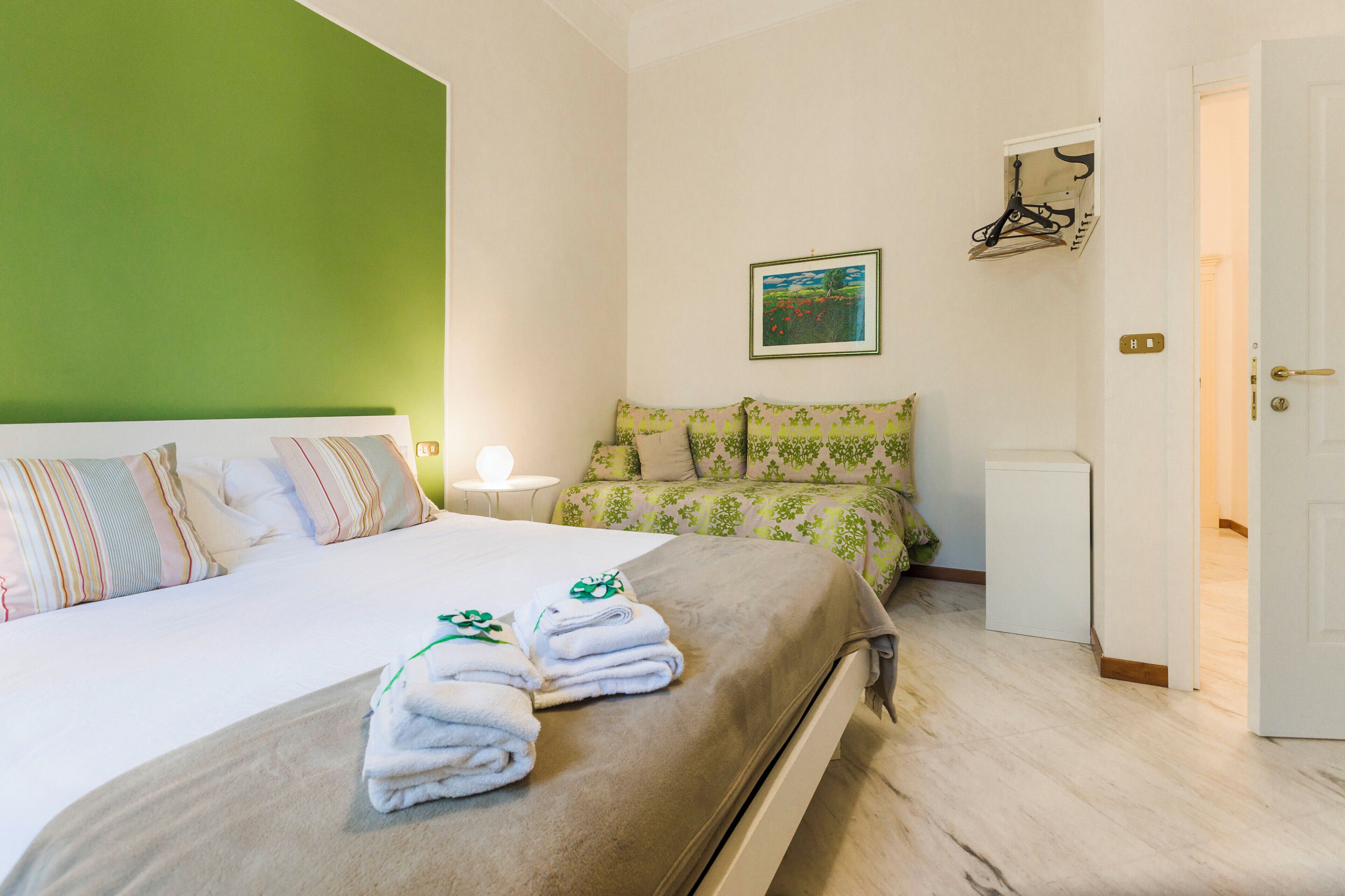 Una camera d'albergo con un letto, un comodino con una lampada, una parete verde e una porta.