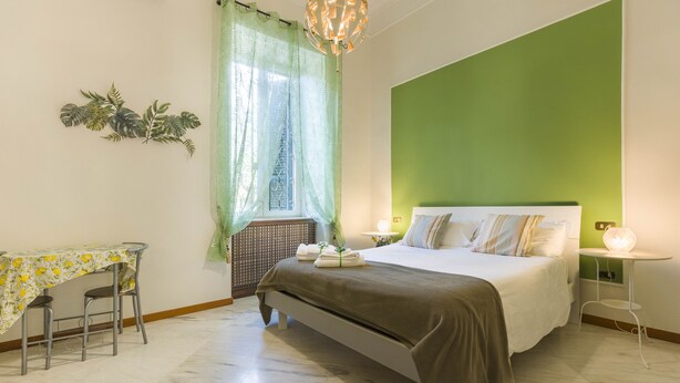 A bedroom with a bed, a table with chairs, a window with curtains, and a green accent wall. - B&B La Casa del Sole a Mergellina (Naples)
