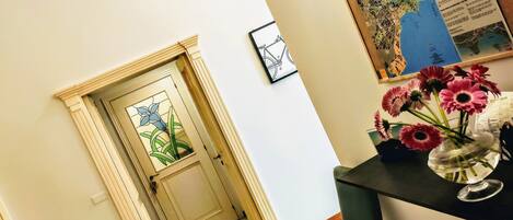 Un pasillo con una puerta que da a una habitación, un mapa enmarcado en la pared y un florero con flores sobre una mesa.