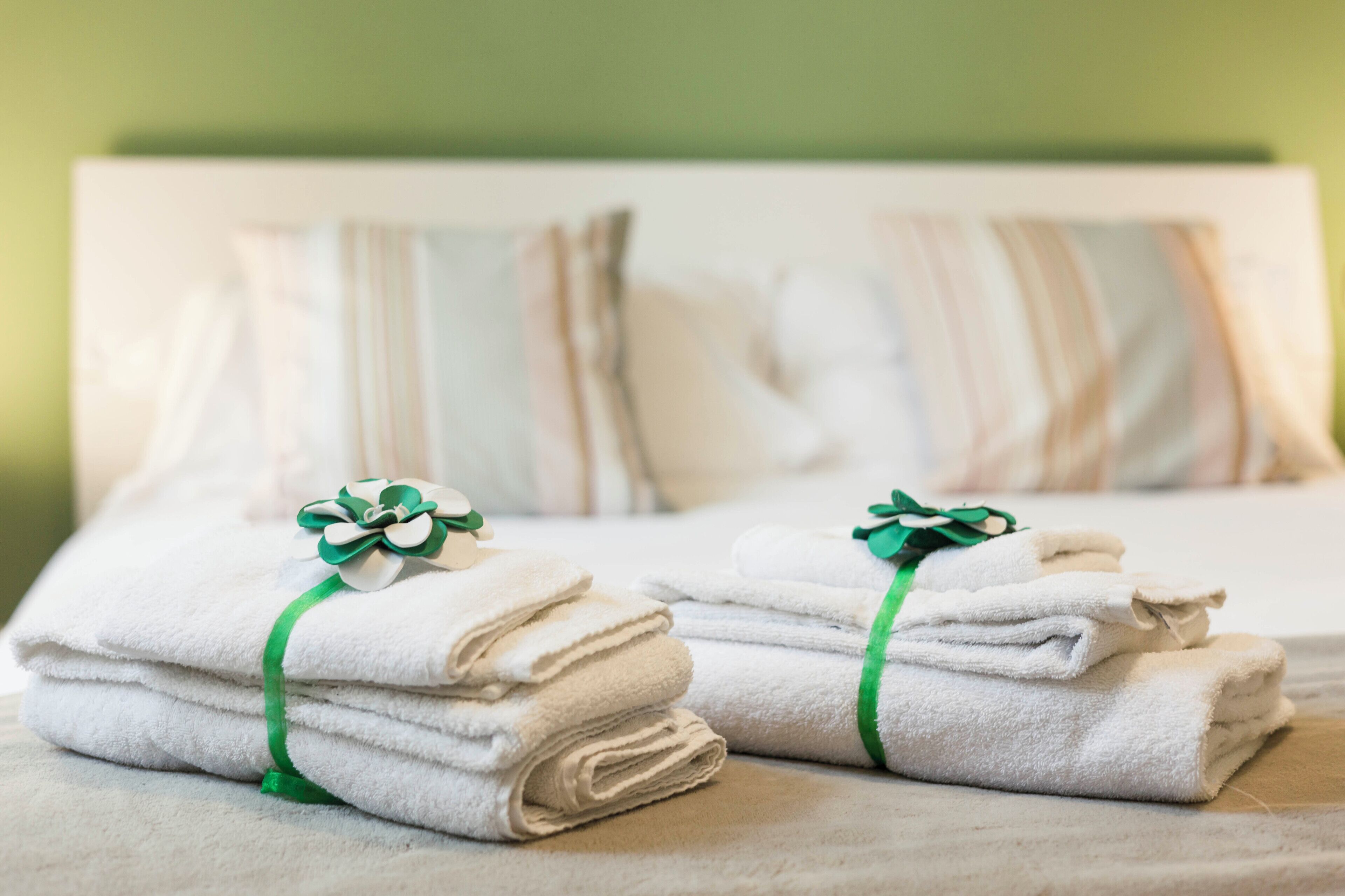 A neatly made bed with white towels and green ribbons, a striped pillow, and a green wall in the background.