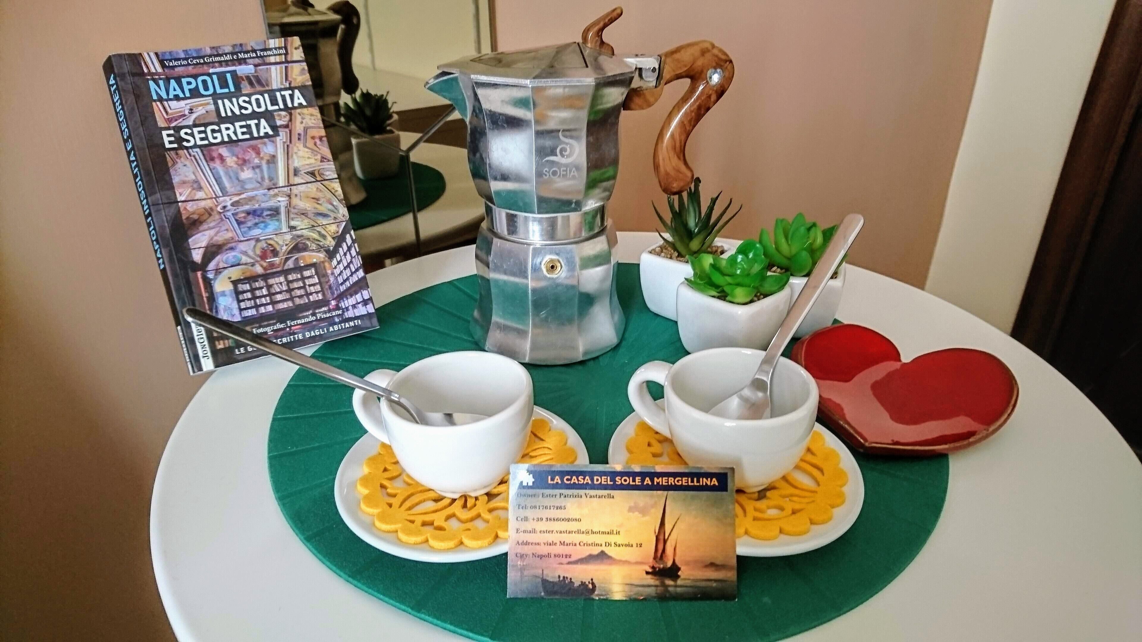 Colazione servita con una caffettiera, tazze e un dolce a forma di cuore su un tavolo.