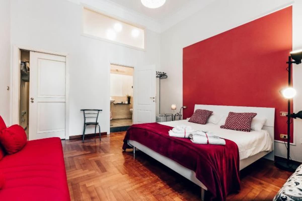A bedroom with a bed, a red wall, a wooden floor, and a closet.