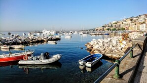 A marina with boats docked, a rocky shoreline, and a cityscape in the background. - B&B La Casa del Sole a Mergellina (Naples)