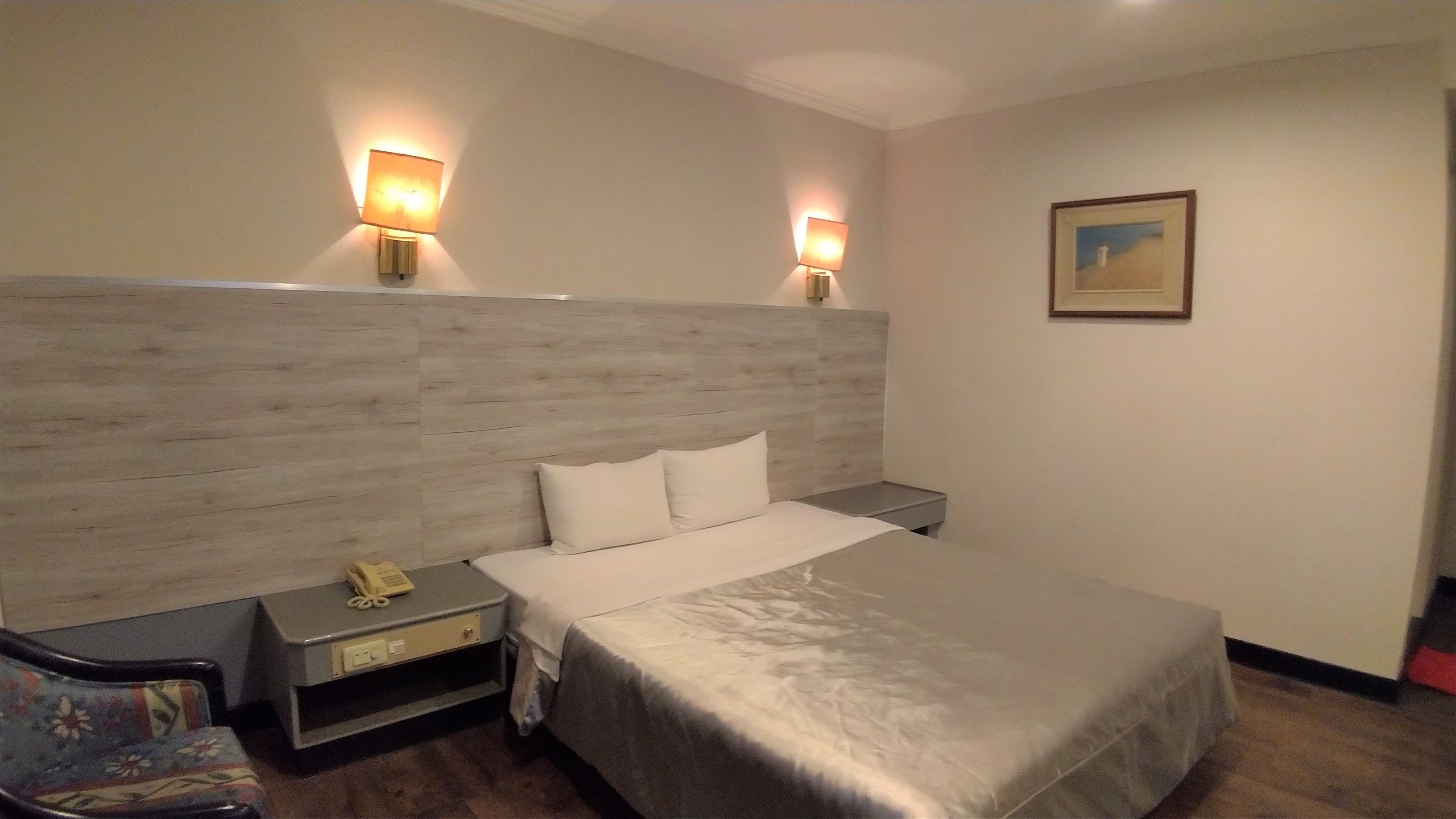Habitación de hotel con una cama grande, dos lámparas de noche, una mesita con teléfono y un cuadro en la pared.