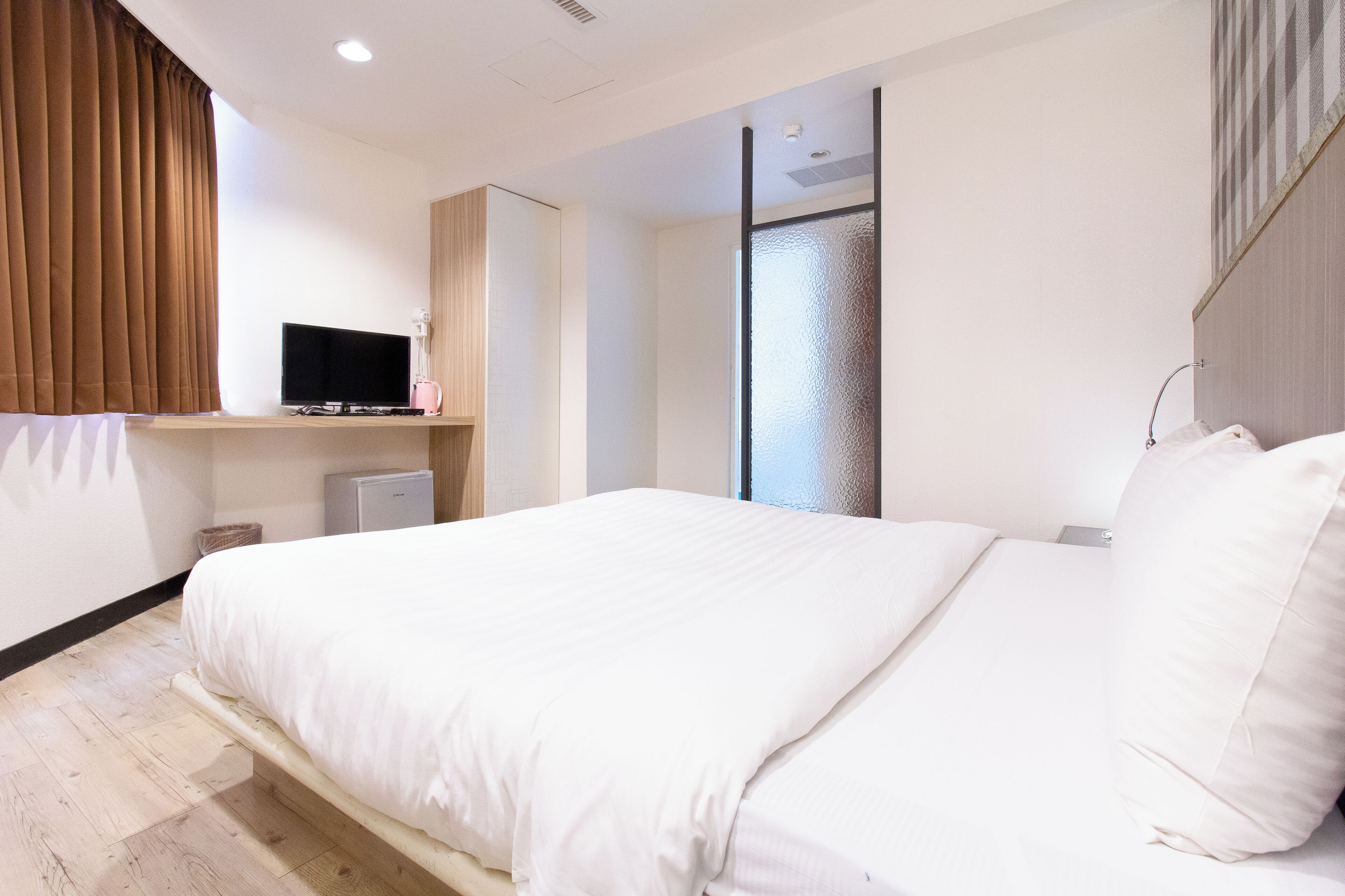 A modern hotel room with a large bed, a flat-screen TV, a small desk, and a wardrobe.