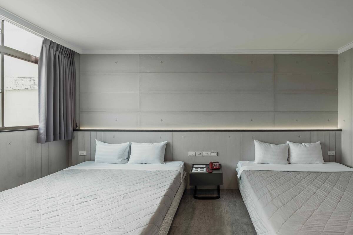 Une chambre d’hôtel avec deux lits, une table de chevet avec un téléphone et une fenêtre avec des rideaux.