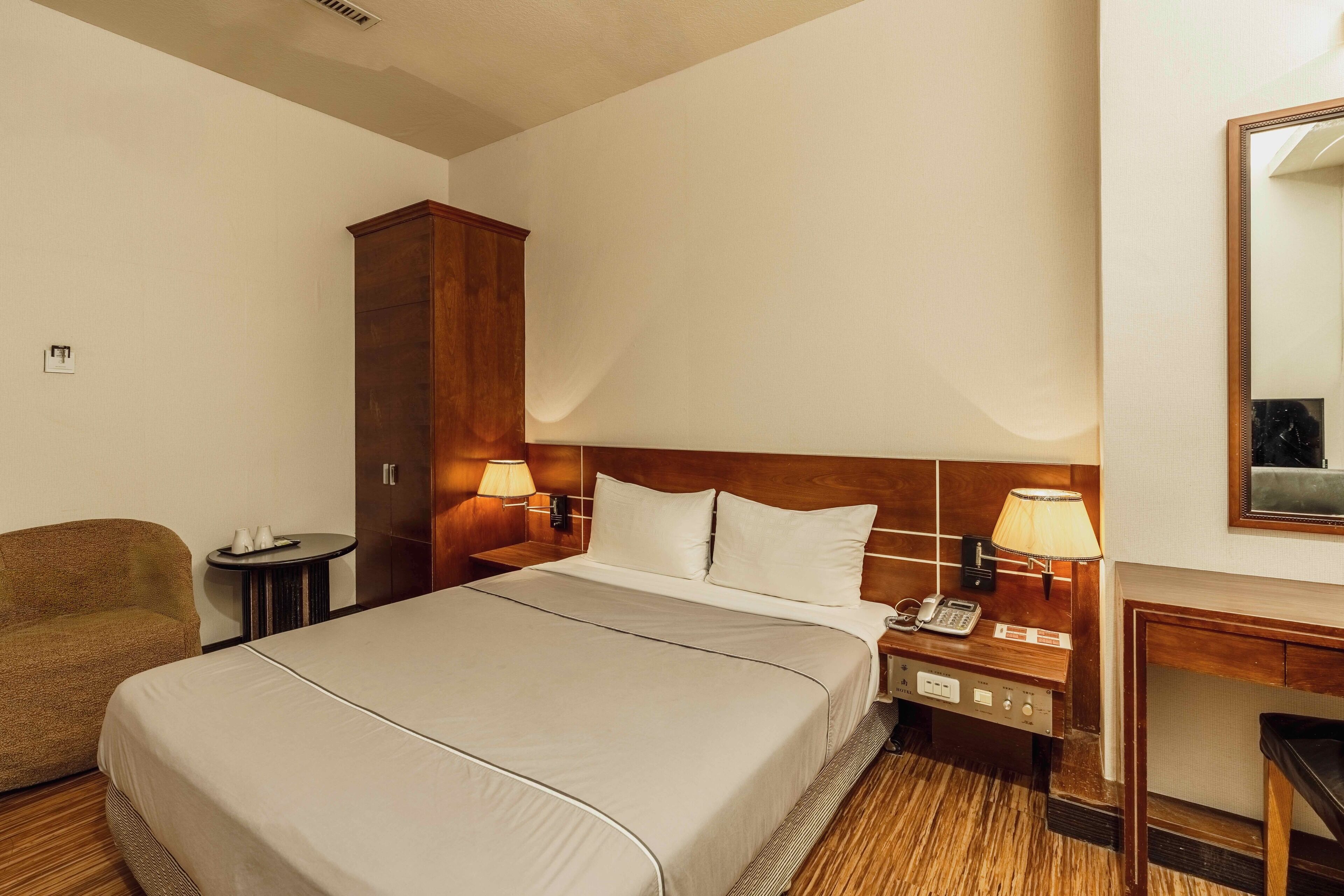 Une chambre d’hôtel avec un grand lit, deux tables de chevet avec des lampes, une armoire en bois, une petite table ronde et une chaise.