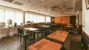 Un comedor amplio con varias mesas y sillas, ventanas grandes que proporcionan luz natural, y una zona de cocina visible al fondo.