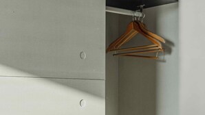 Un rincón de una habitación con pared blanca, un perchero de madera y un estante metálico.