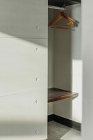 Un rincón de una habitación con pared blanca, un perchero de madera y un estante metálico.