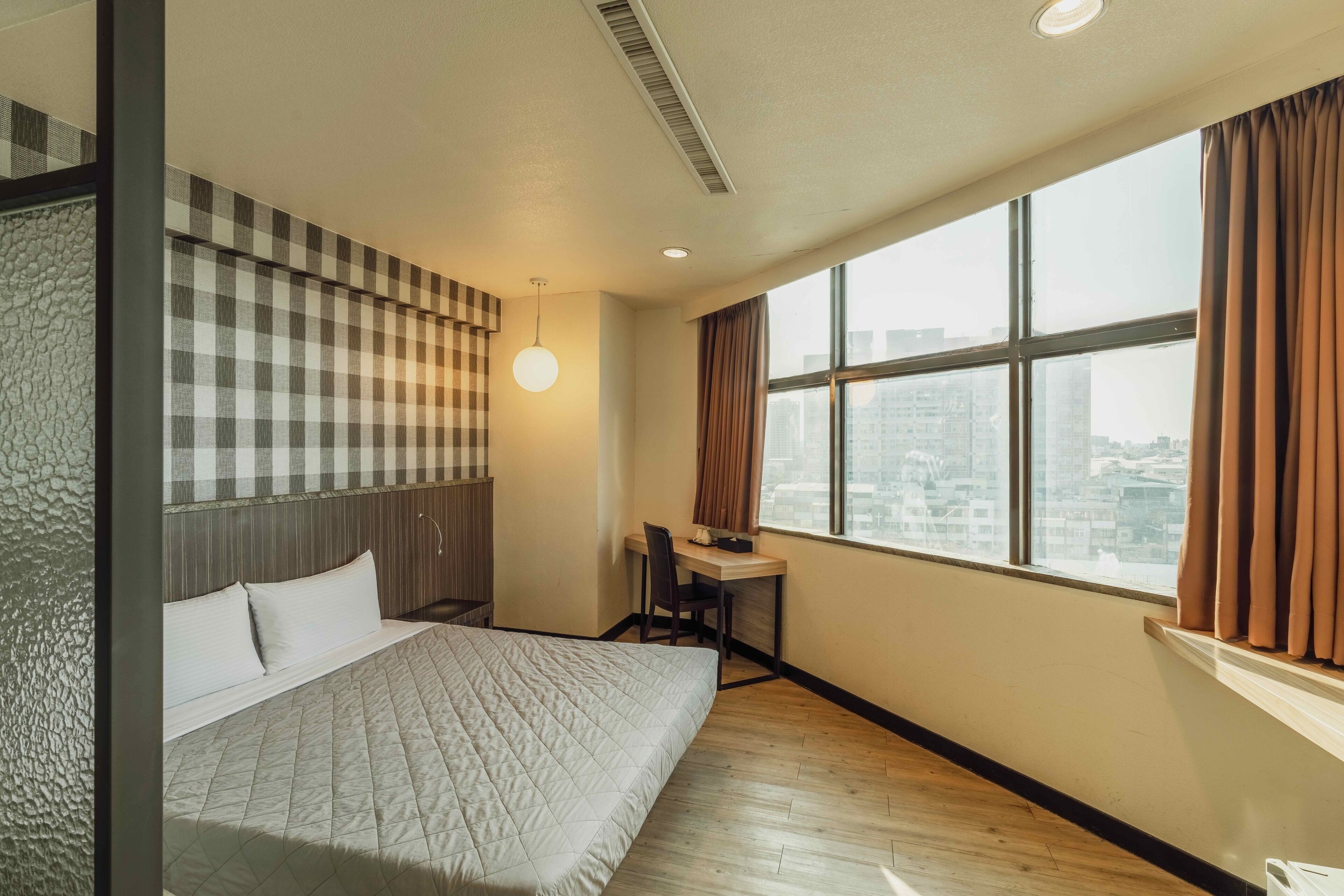A hotel room with a bed, a desk, and a large window with curtains.