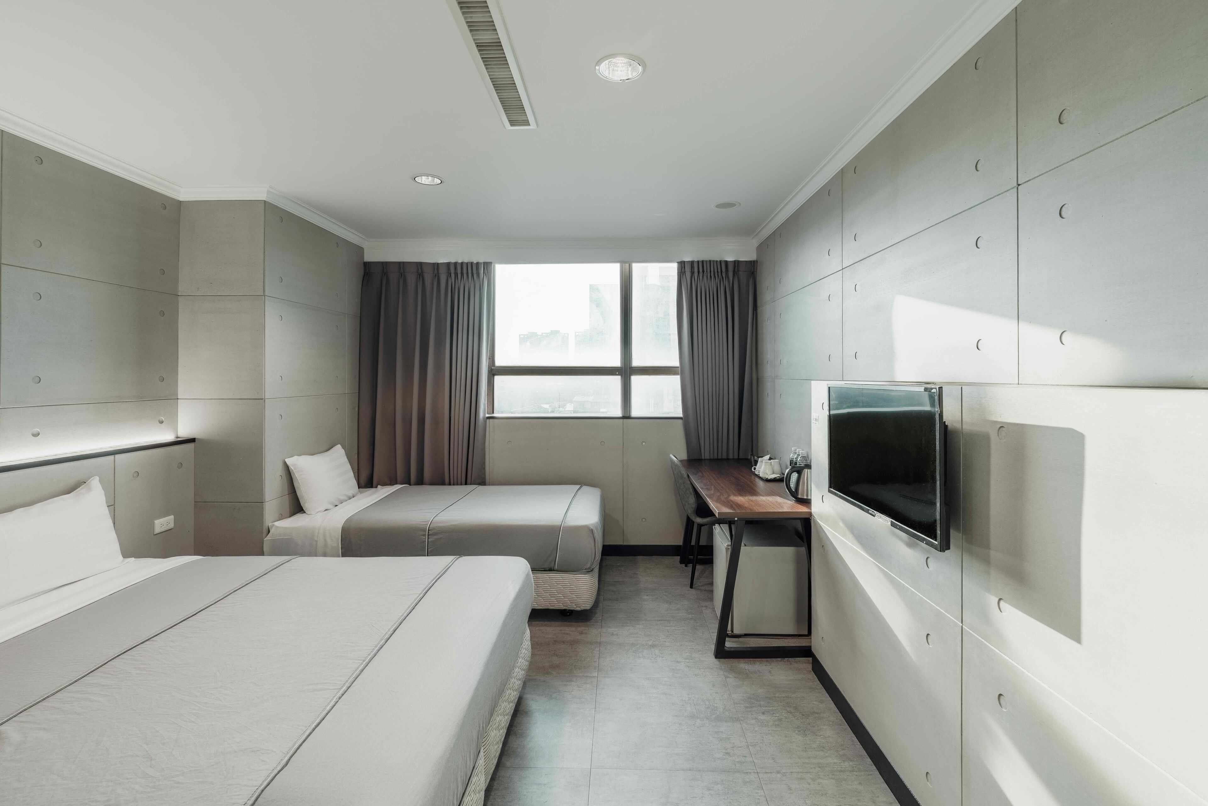 Habitación de hotel con dos camas, un escritorio con televisor y una ventana con cortinas.