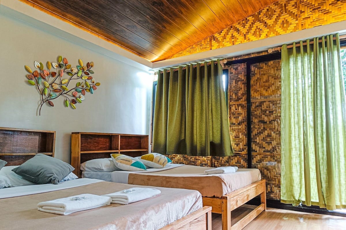 Une chambre avec deux lits, un plafond en bois, une décoration murale représentant des motifs de feuilles et des rideaux verts.