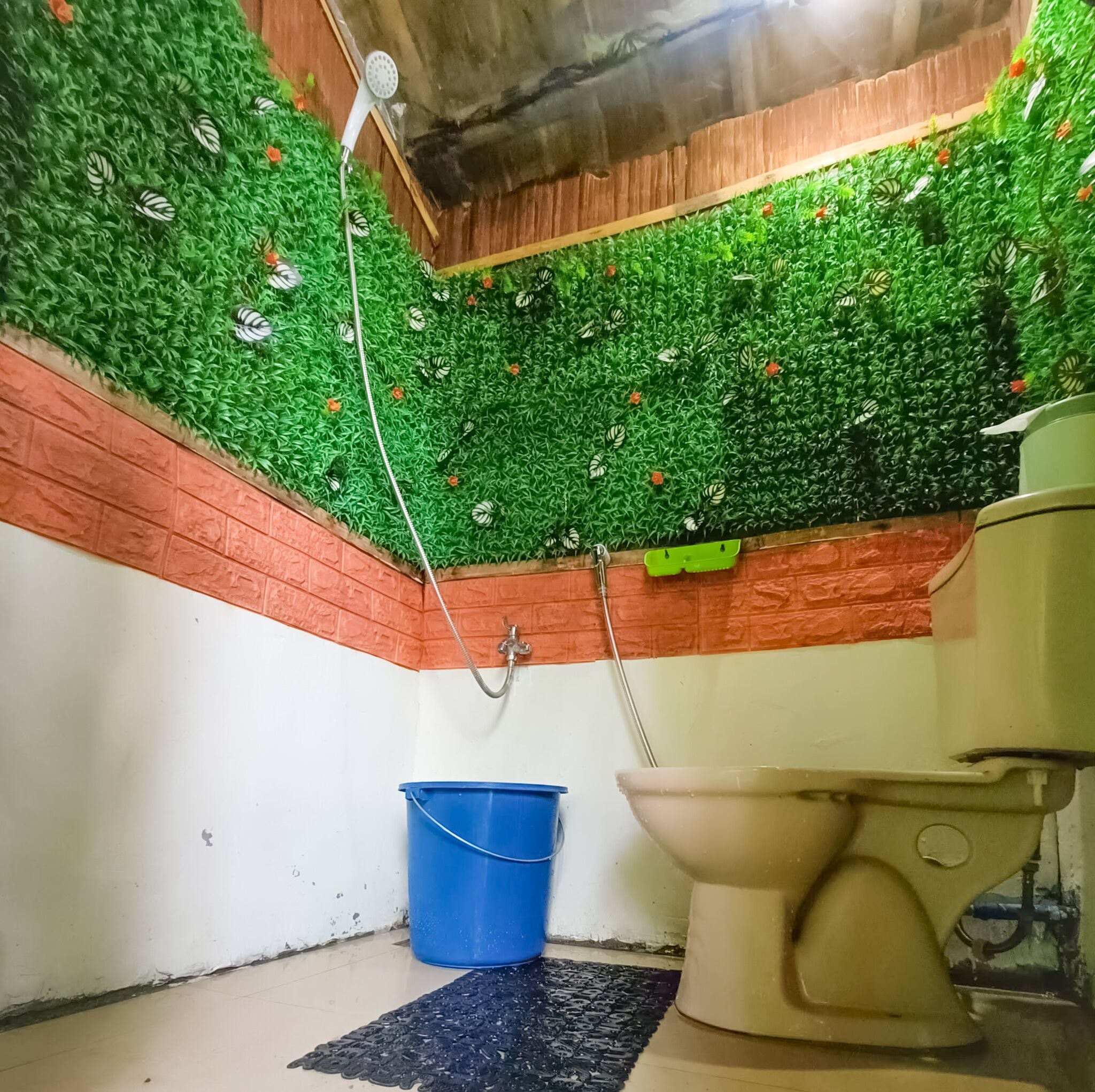A bathroom with a green artificial grass ceiling, a blue bucket, and a beige toilet.