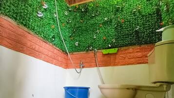 A bathroom with a green artificial grass ceiling, a blue bucket, and a beige toilet.