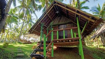 A traditional bamboo structure with a thatched roof, surrounded by palm trees.