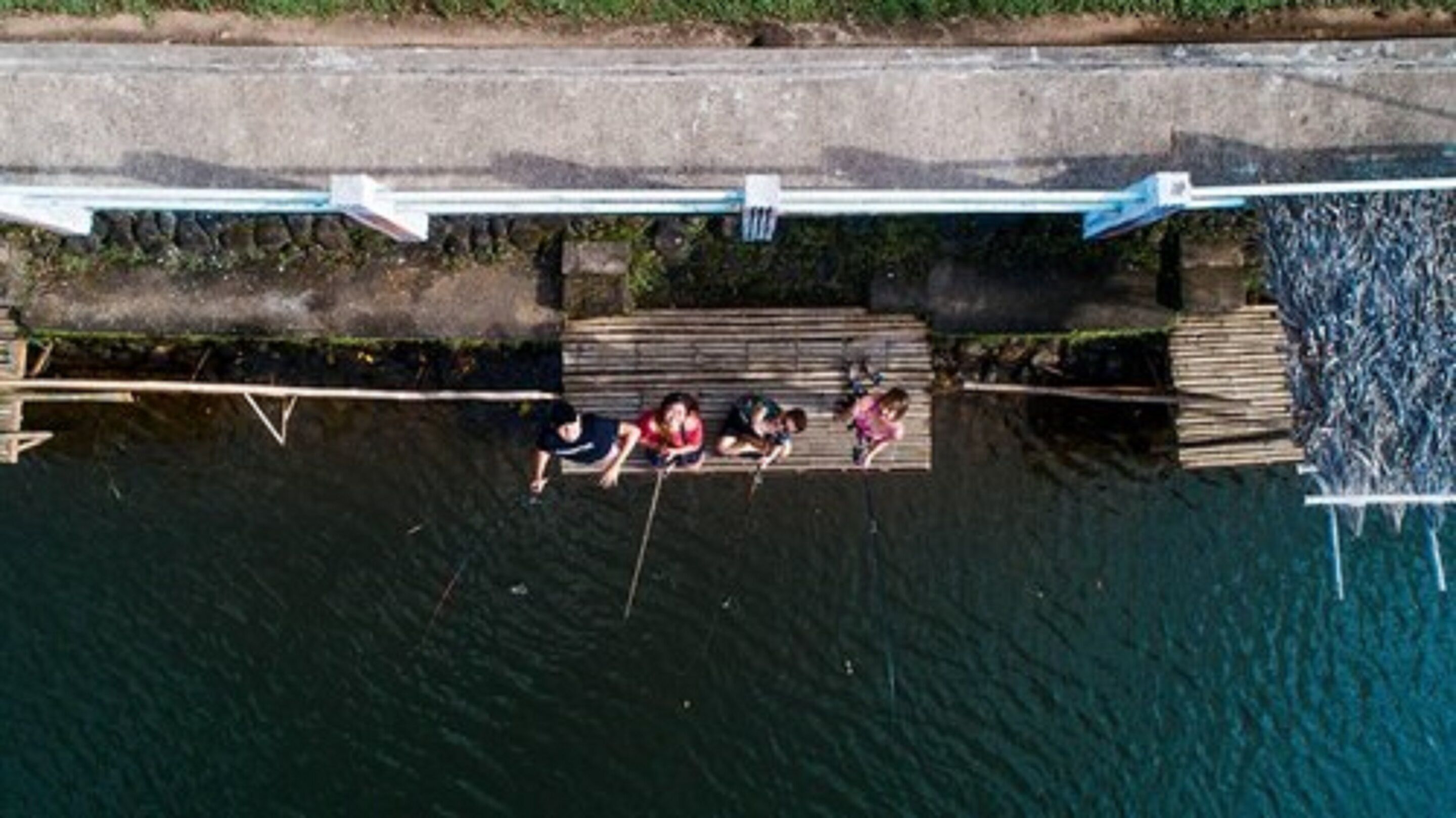 A wooden dock extending over a body of water, with a bridge in the background.