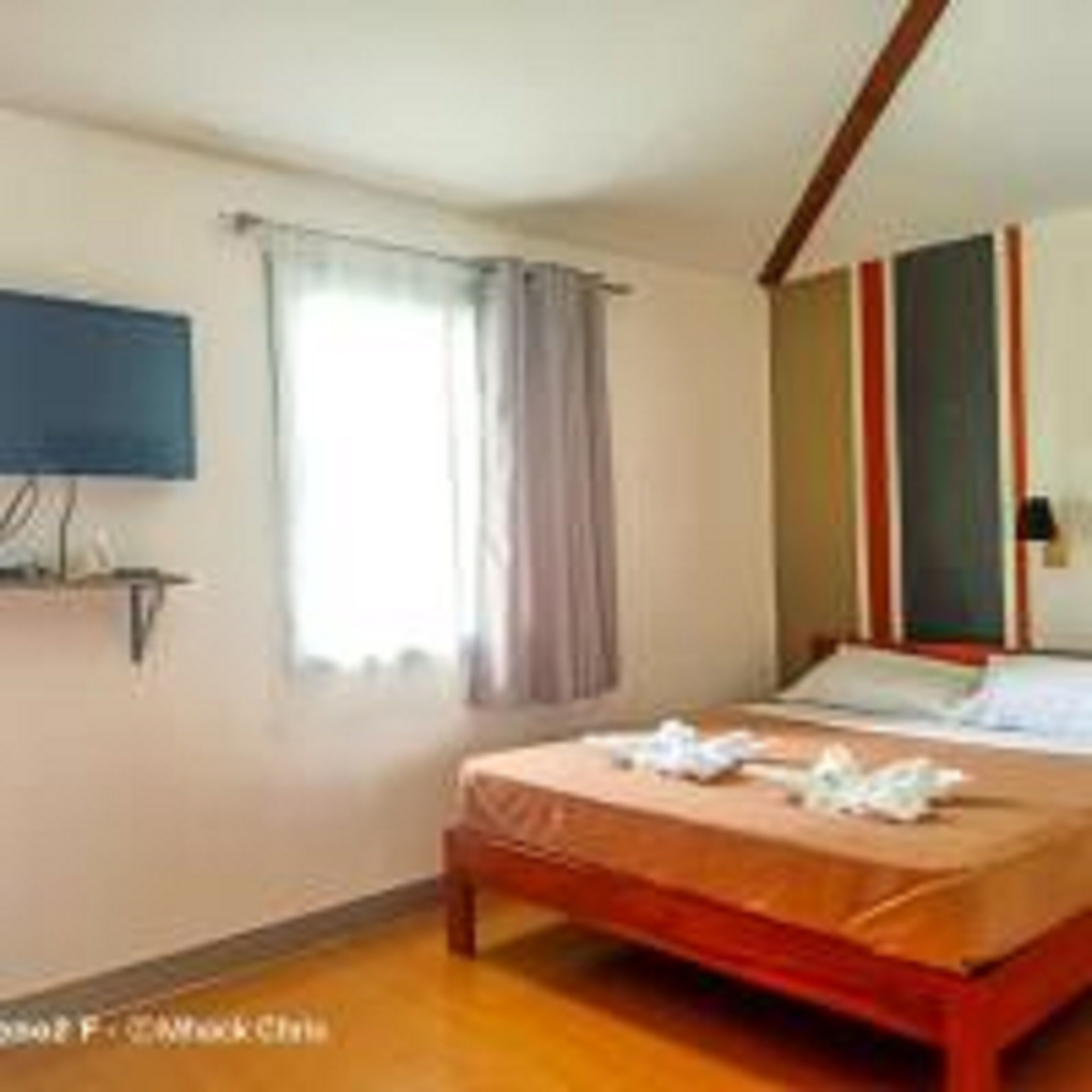 Un dormitorio con cama, televisor montado en la pared y ventana con cortinas.