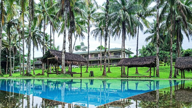 A swimming pool with a reflection of palm trees and a building in the background. - Caliraya Ecoville Recreation and Farm Resort (Cavinti)