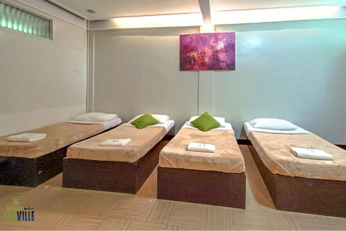 Une chambre d’hôtel avec quatre lits simples disposés en rangée, chacun étant muni d’un oreiller et d’une serviette pliée.