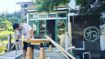 A person working on a wooden structure outdoors, possibly a deck or platform, with a building in the background.