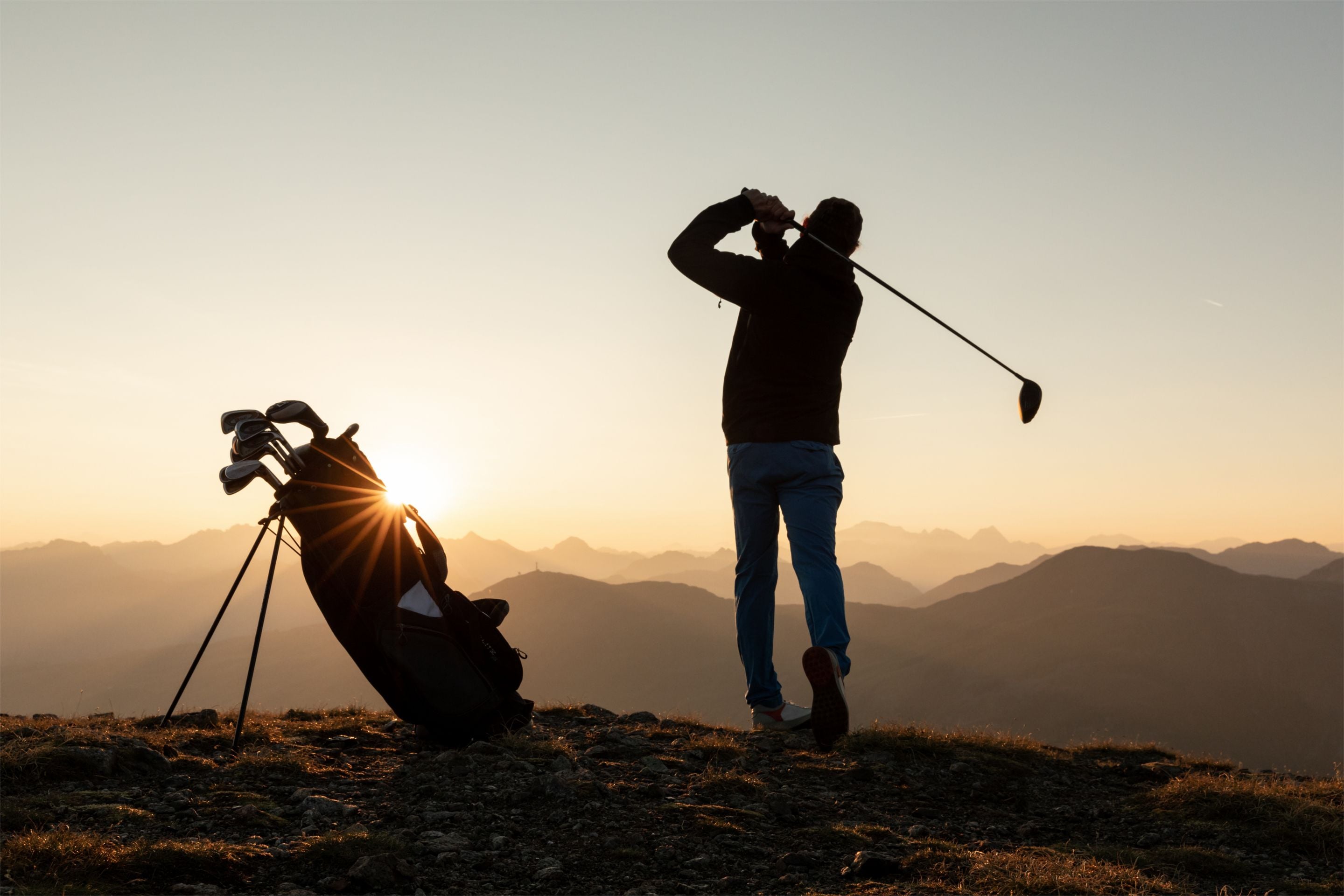 A person golfing on a mountain with a golf bag and a tripod in the foreground.
