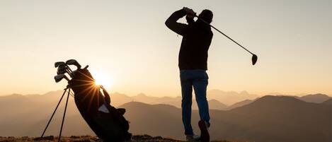 A person golfing on a mountain with a golf bag and a tripod in the foreground.