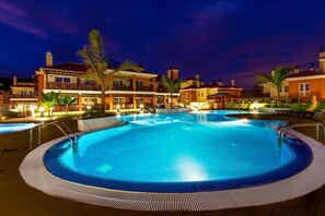A swimming pool surrounded by buildings with balconies, palm trees, and a night sky. - La Casa Canaria (Mogan)