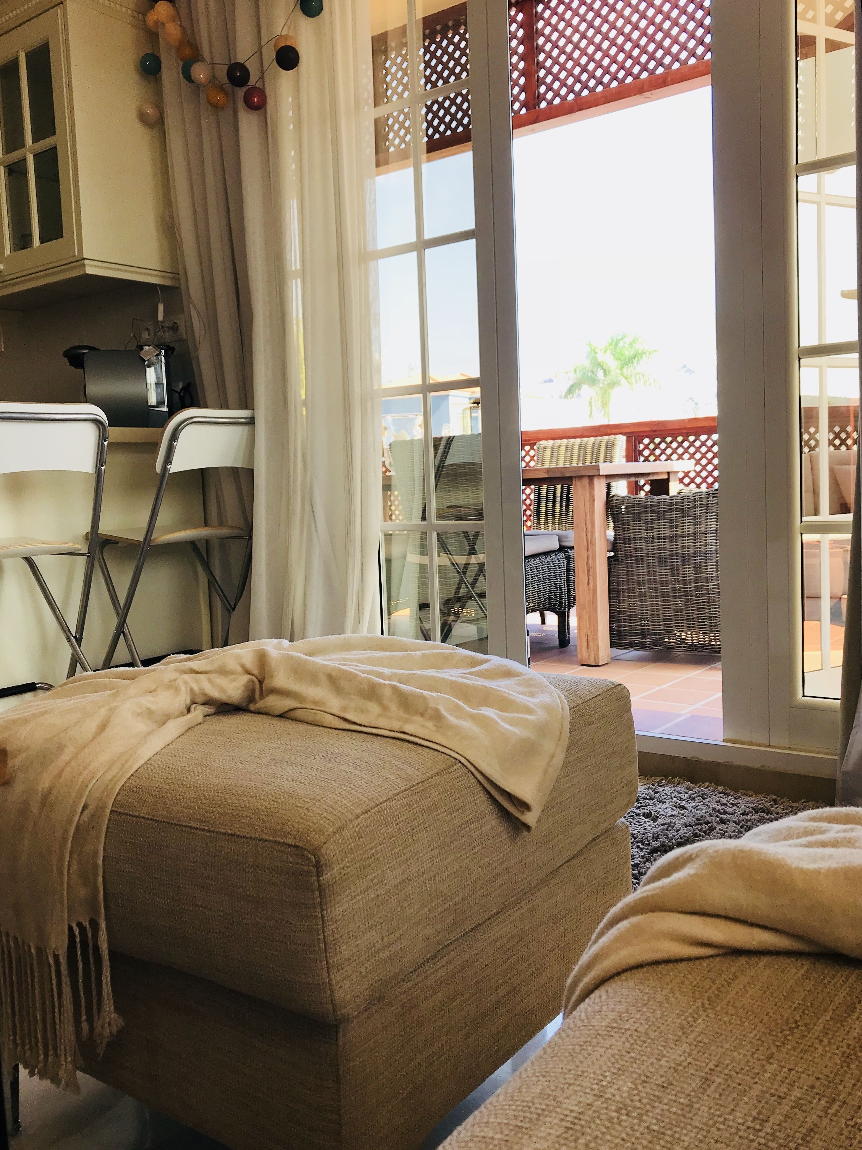 Ein gemütlicher Wohnbereich mit einer Couch, einem kleinen Tisch und einem Sessel. Ein großes Fenster bietet einen Blick ins Freie.