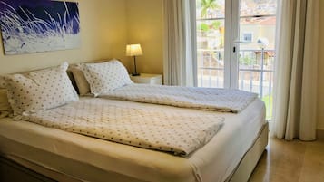 A double bed with star-patterned bedding, a bedside lamp, and a view of a balcony with buildings and palm trees.