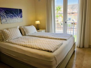 A double bed with star-patterned bedding, a bedside lamp, and a view of a balcony with buildings and palm trees. - La Casa Canaria (Mogan)