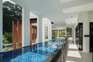 Una piscina interior moderna con baldosas azules cristalinas, rodeada de pilares blancos y puertas de vidrio que dan a una zona de recepción.