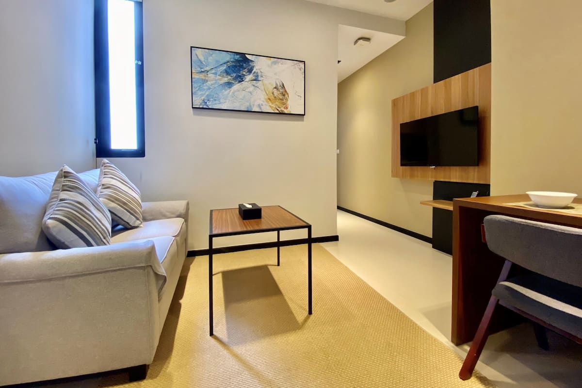 Ein modernes Wohnzimmer mit einer Couch, einem Couchtisch, einem an der Wand befestigten Fernseher und einem Essbereich mit Tisch und Stühlen.