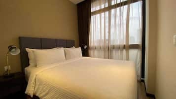 A neatly made bed with a headboard, a bedside lamp, and a window with sheer curtains.