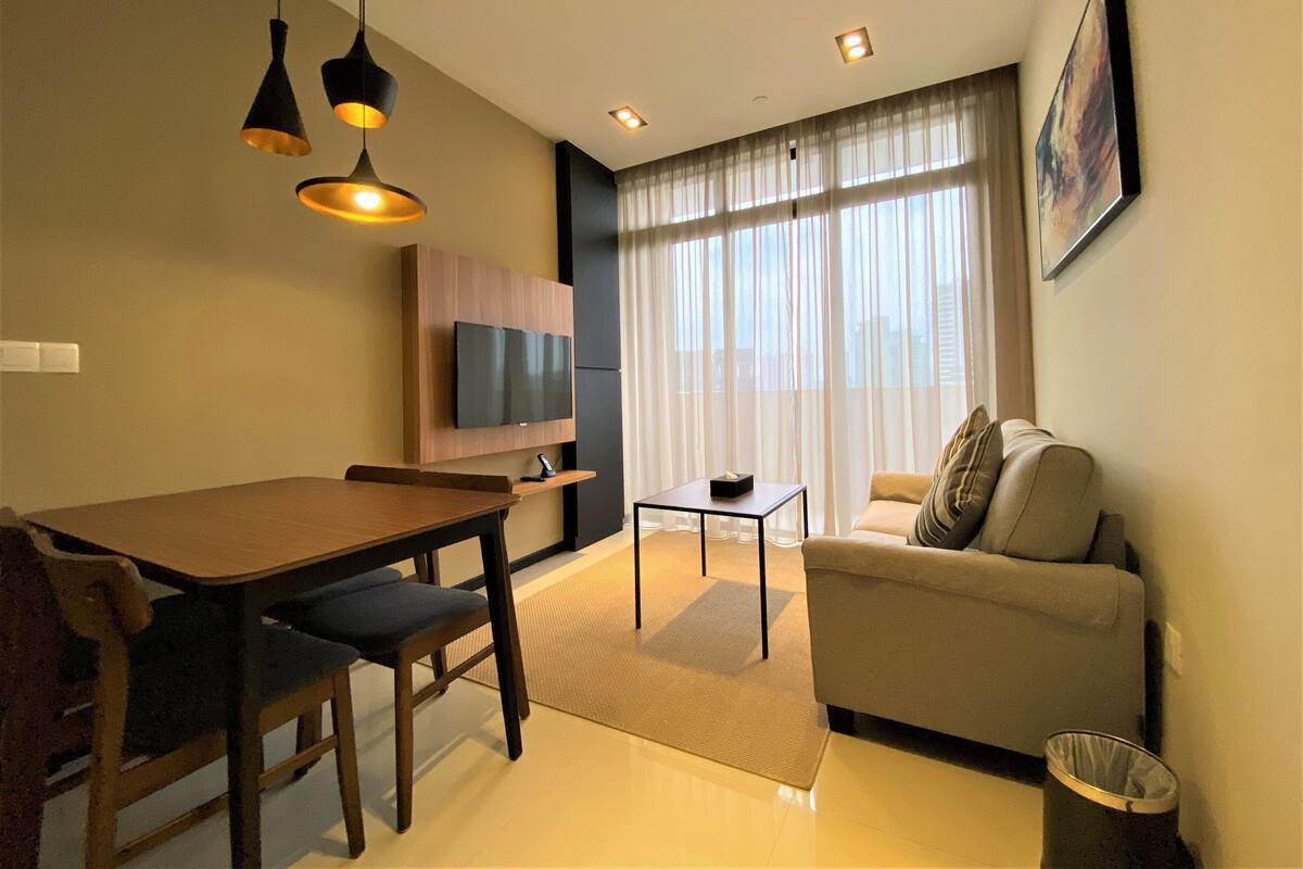 A modern living room with a dining table, sofa, TV, and large windows.