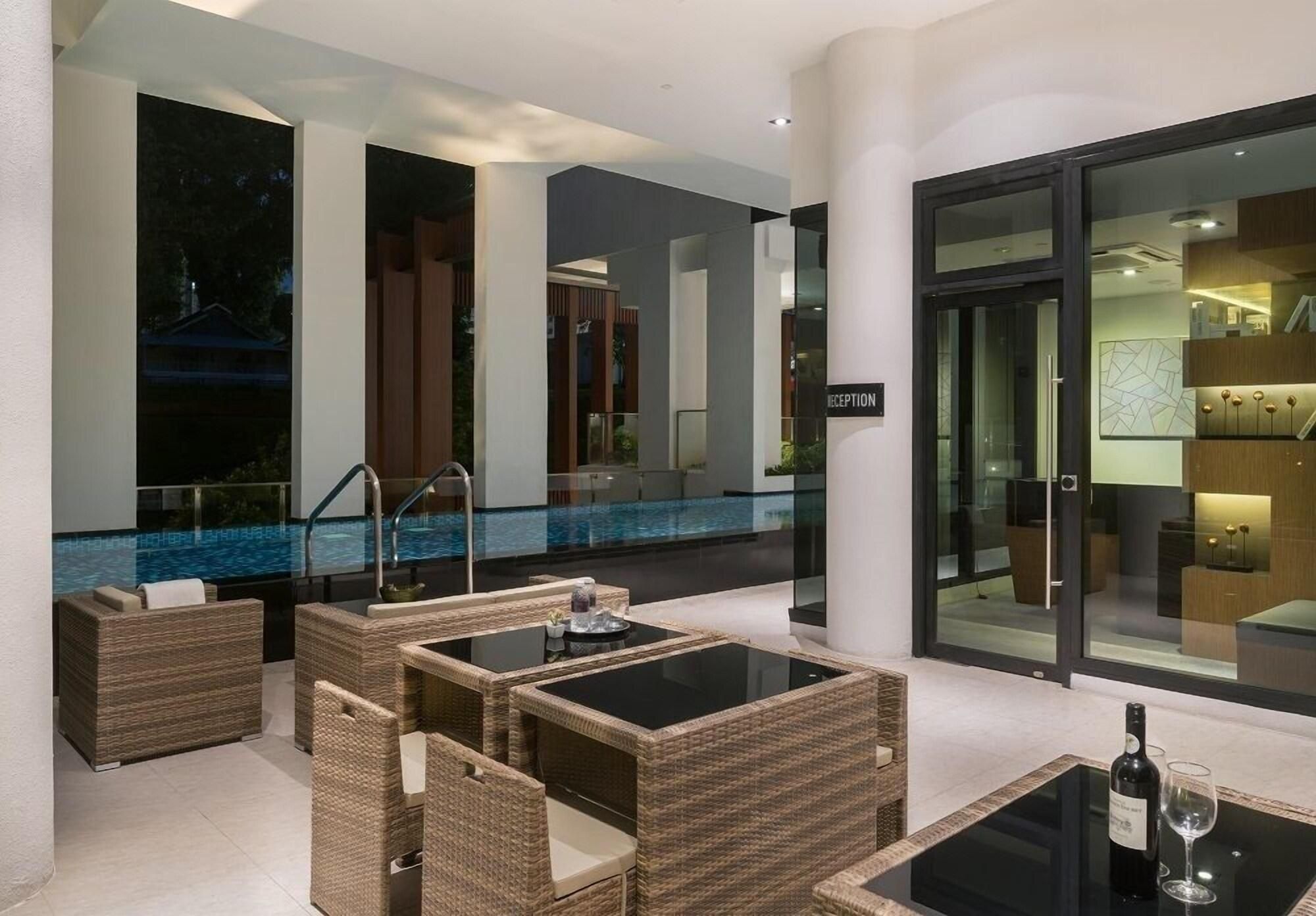 A modern outdoor lounge area with wicker furniture, a glass table, and a pool in the background.