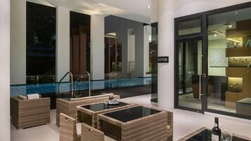 A modern outdoor lounge area with wicker furniture, a glass table, and a pool in the background.