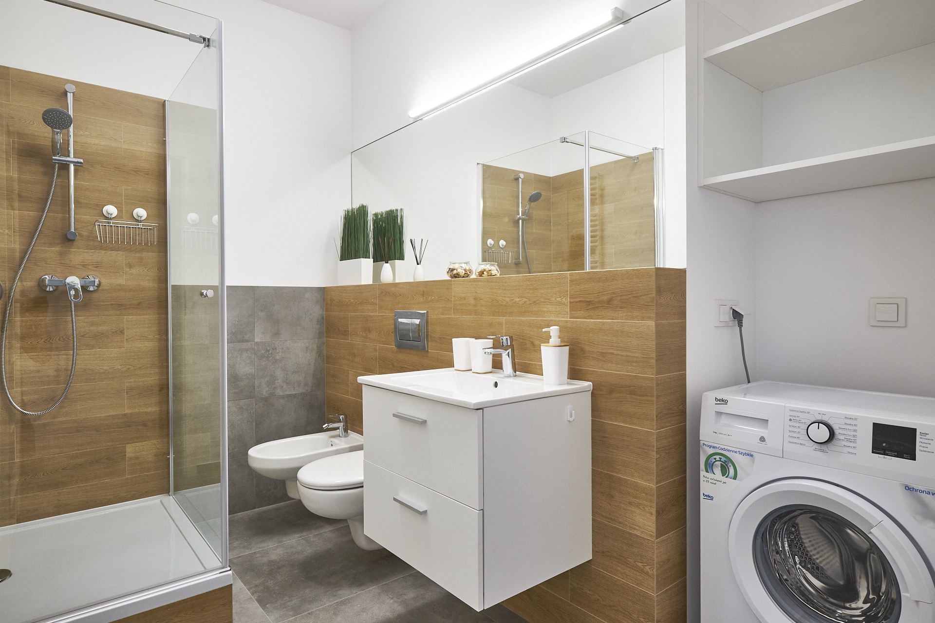 A modern bathroom with a glass shower enclosure, a toilet, a sink with a mirror, and a washing machine.