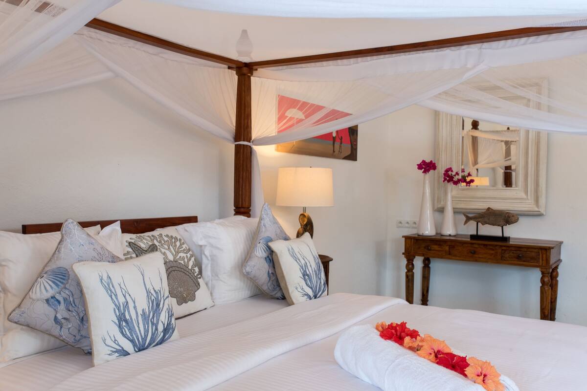 Una habitación de hotel con cama con dosel, una mesita de noche con lámpara y un espejo en la pared.