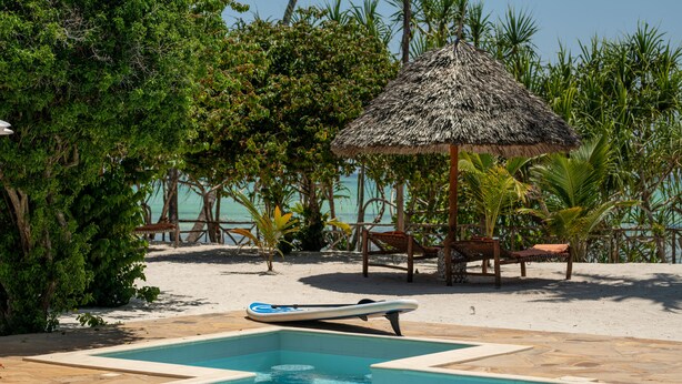 A pool area with a thatched umbrella, lounge chairs, and a small boat. - Tikitam Palms Boutique Hotel (Kiwengwa)