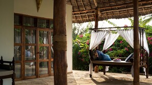 A wooden bench with cushions and a canopy, a wooden chair, and a glass door with curtains. - Tikitam Palms Boutique Hotel (Kiwengwa)