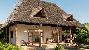A thatched-roof bungalow with a wooden porch, a wooden chair, and a table. - Tikitam Palms Boutique Hotel (Kiwengwa)