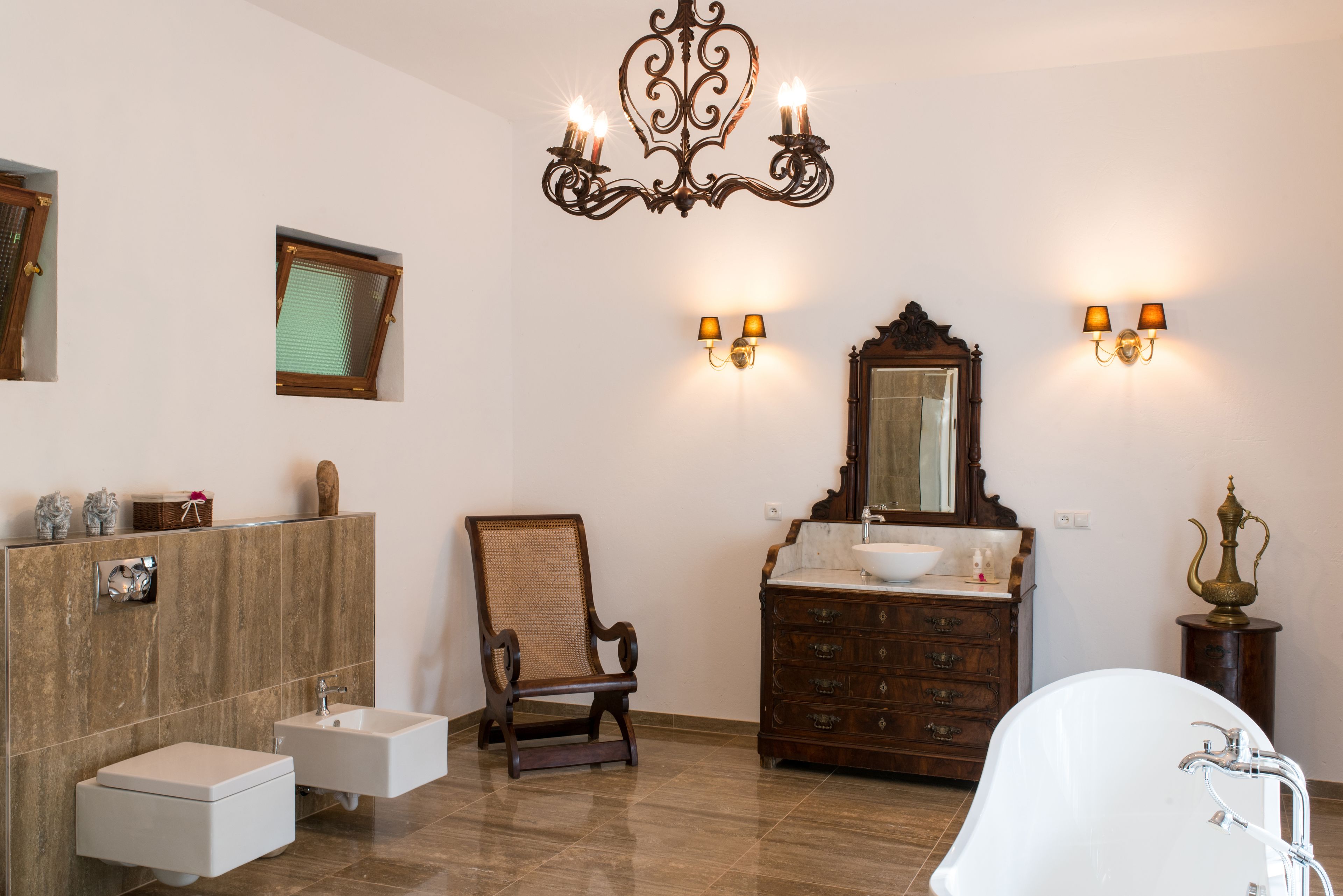 A bathroom with a wooden chair, a large mirror, a white bathtub, and a chandelier.