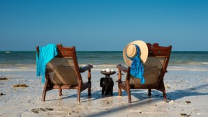 Two wooden beach chairs with blue towels and hats, a small table with decorative items, and the ocean in the background. - Tikitam Palms Boutique Hotel (Kiwengwa)