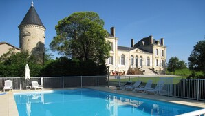 A swimming pool with lounge chairs and umbrellas, a stone tower, and a large building with arched windows.