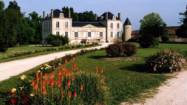 A large, historic building with a symmetrical facade, a central tower, and a formal garden with a gravel path.